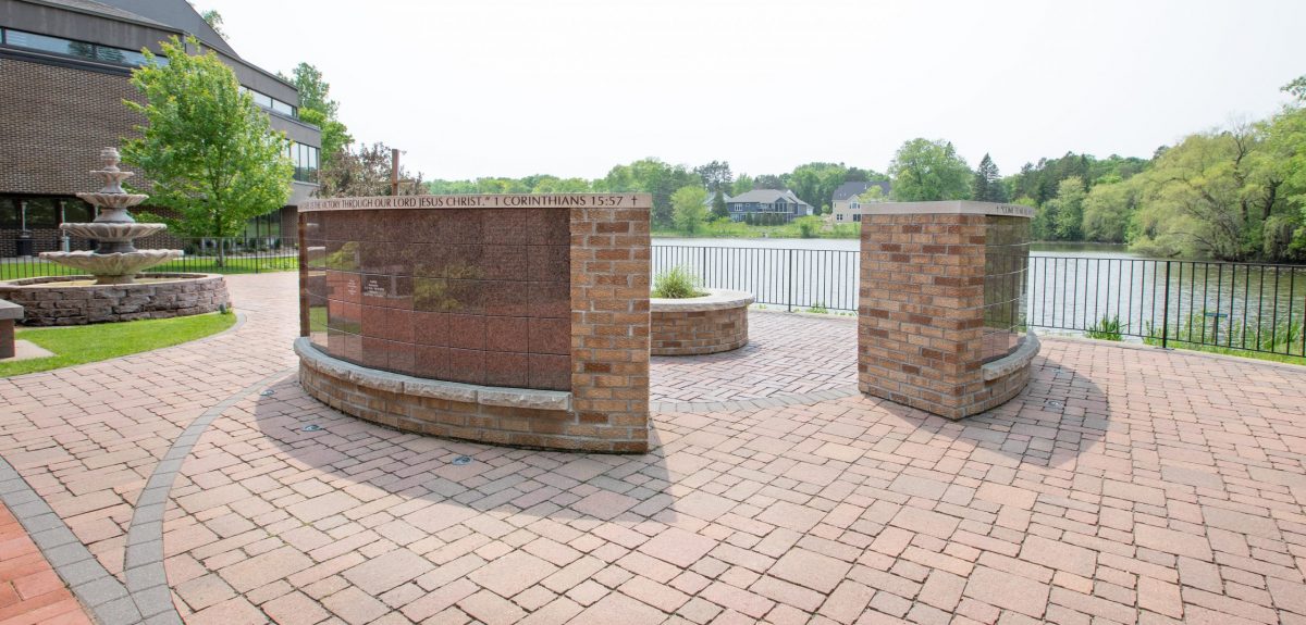 A memorial space in close proximity to a church is encompassed with a handrail and overlooks a serene lake.