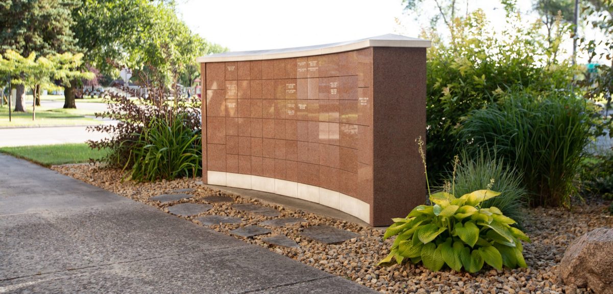Attractive plantings surround a columbarium wall in a bed of loose rock and stepping stones.