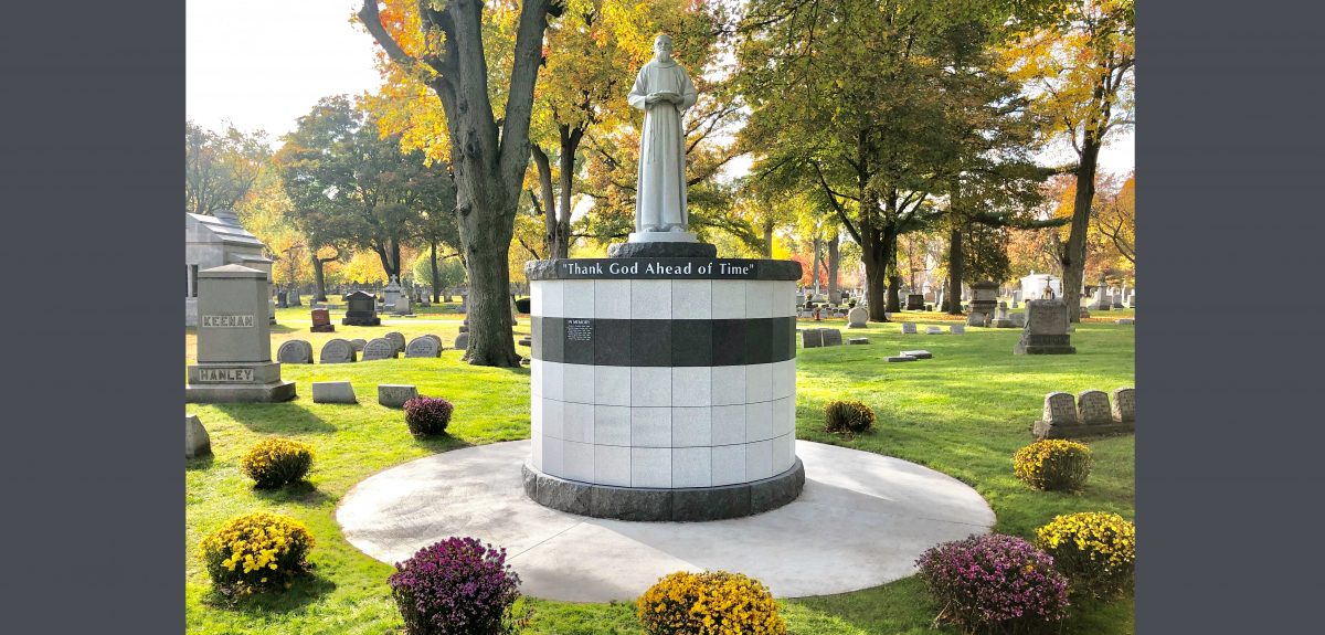 A York Ossuarium is adorned with a statue of Father Solanus Casey in historic cemetery setting.