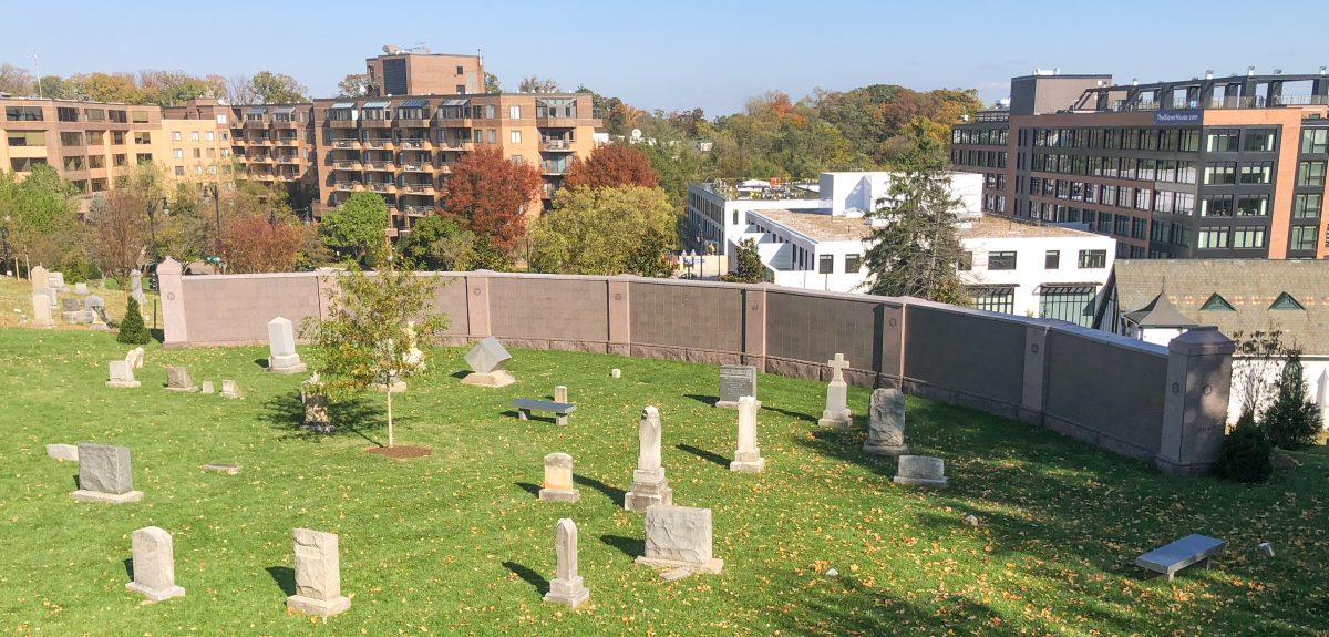 A cemetery and city skyline are separated by a seven panel curved wall columbarium.