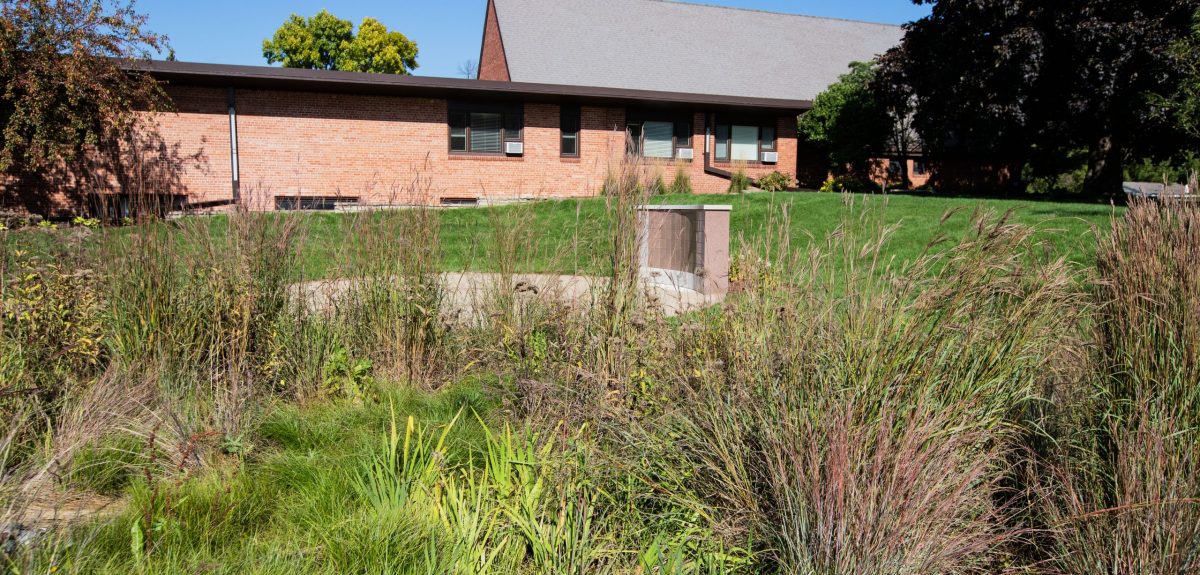 A wall columbarium and church building can be seen behind various thriving plantings.