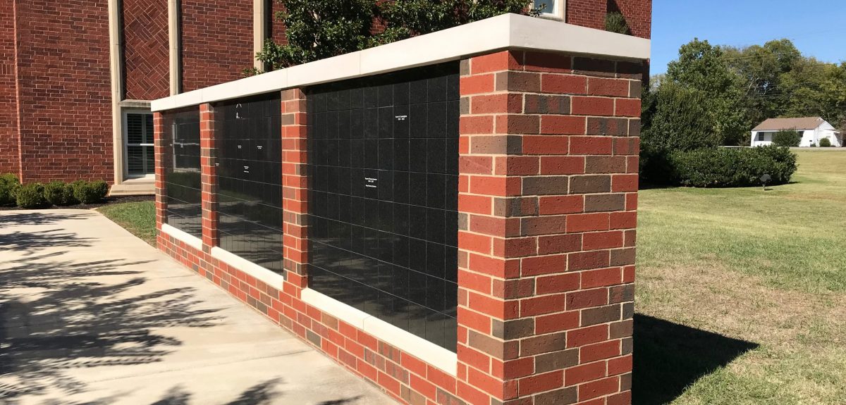 Brick masonry surrounds three niche cabinets clad in granite outside a brick church building.