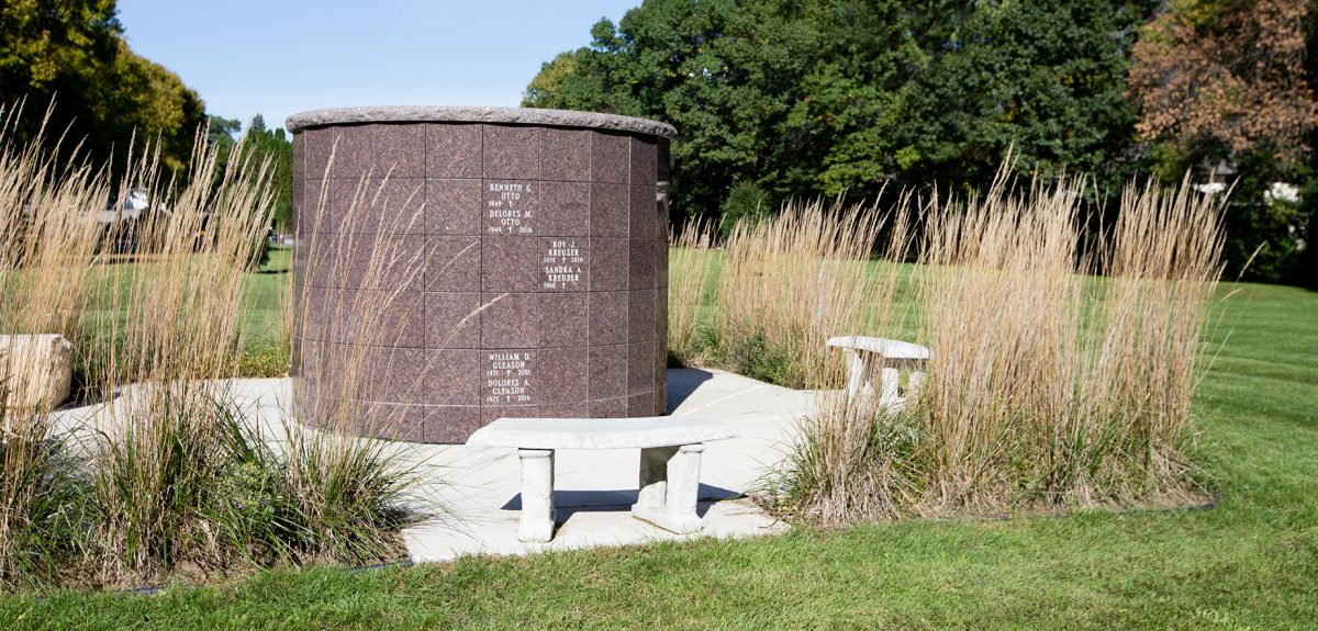 A concrete bench sits in front of a York columbarium surrounded by decorative plantings of feather reed grass.