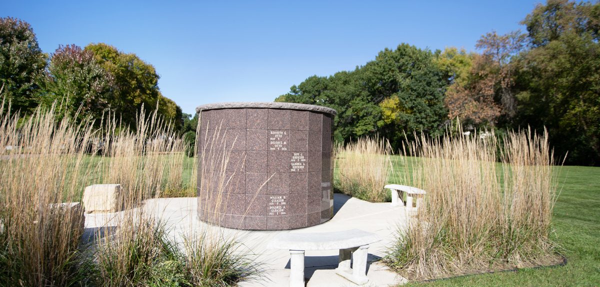 A bright blue sky floats above a grassy clearing that contains a pronounced memorial space.