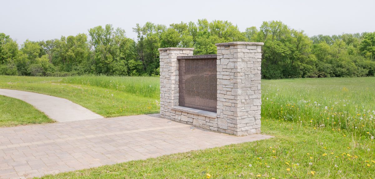A columbarium wall sits on the edge of a field and dense tree line.
