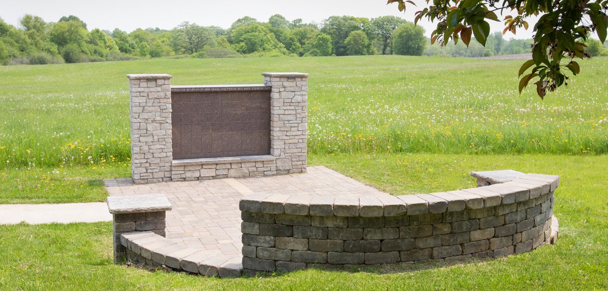 A semicircular retaining wall made of stone brick sits across from a rectangular columbarium wall.