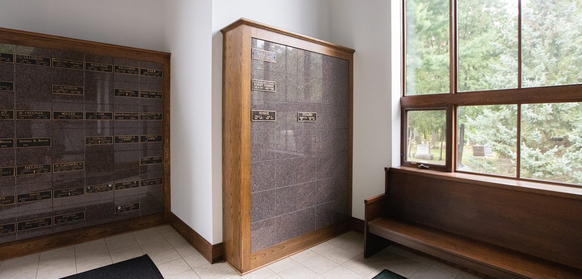Bright sunlight shines in from behind a pew to wash a columbarium cabinet in light.