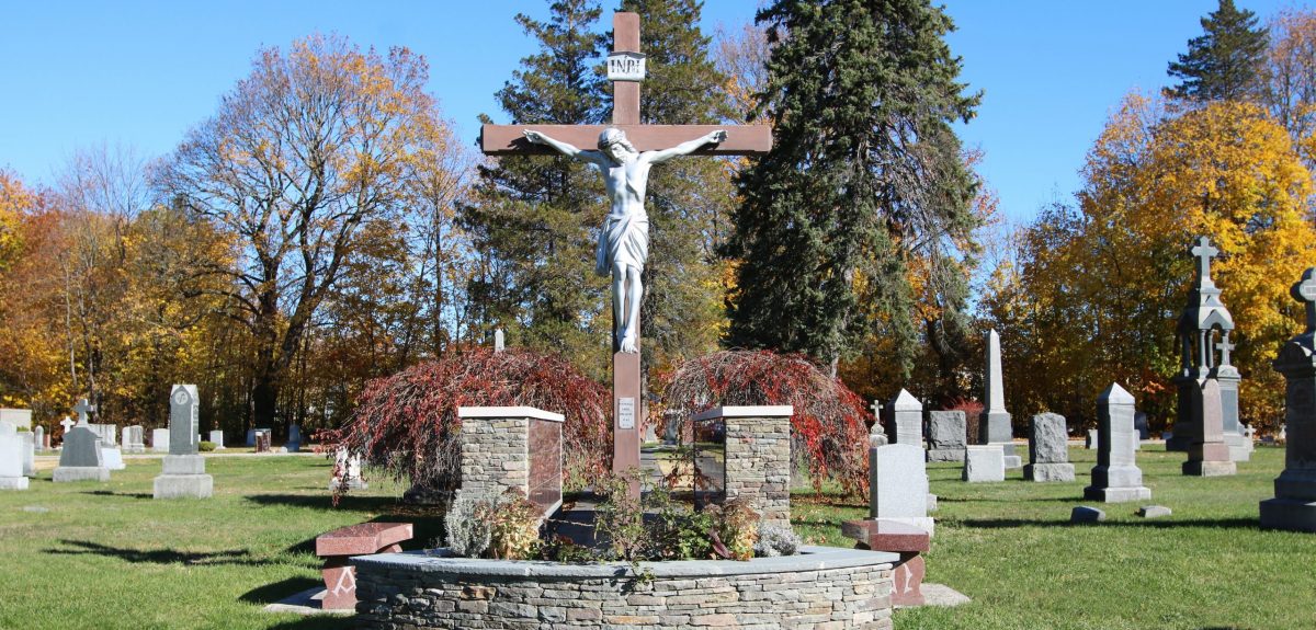 Within a multitude of headstones a large crucifix stands tall over two columbarium walls and matching granite benches.