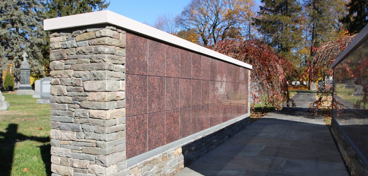 A long and partially shaded cement path separates two identical columbarium walls.