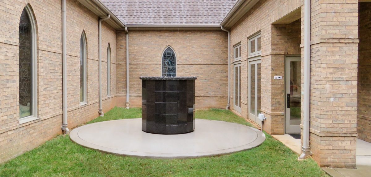A circular concrete pad raises a Winchester columbarium above a lush bed of grass.