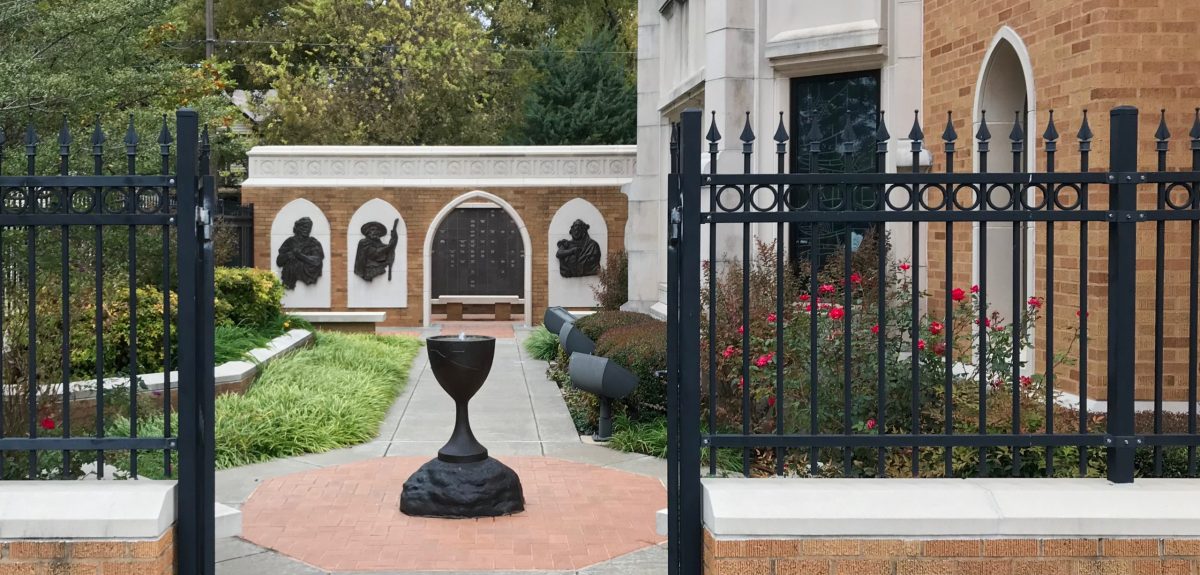 Beyond an ornate, open gate a pathway leads through a lush garden to a semi enclosed columbarium space.
